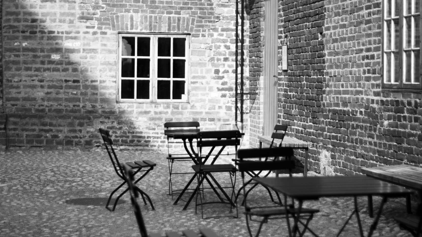 a black and white photo of tables and chairs in a courtyard, a black and white photo, realism, brick, restaurant menu photo