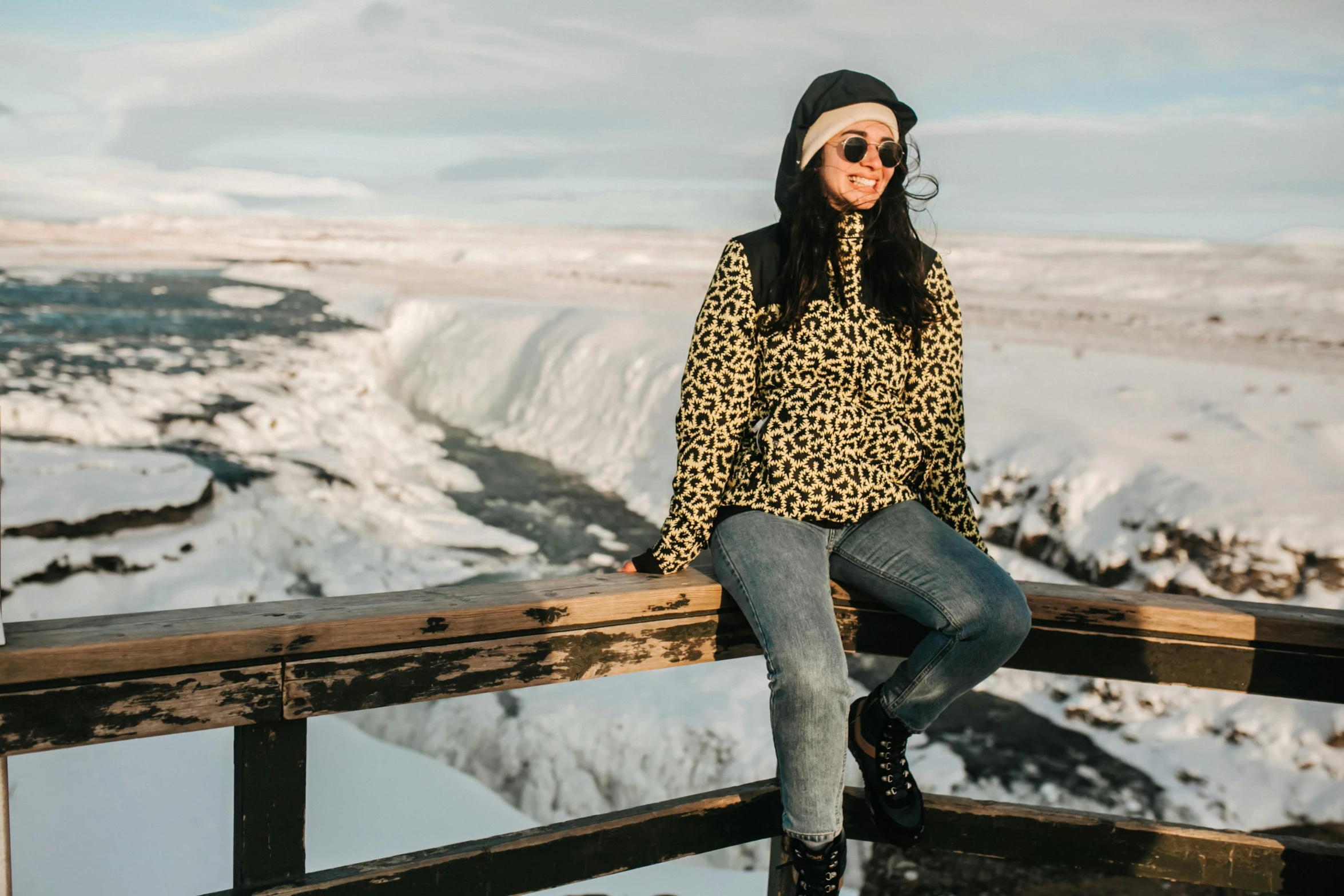 a woman sitting on a railing in front of a waterfall, inspired by Louisa Matthíasdóttir, trending on pexels, hurufiyya, snow leopard, wearing sunglasses and a cap, in an igloo, patterned clothing