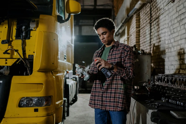 a man standing in front of a yellow truck, pexels contest winner, holding a battery, inspect in inventory image, male teenager, in a workshop