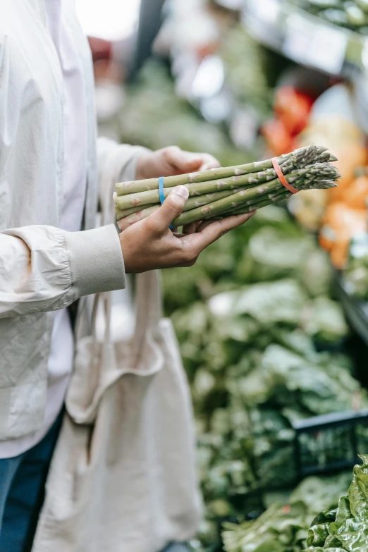 a woman is holding a bundle of asparagus, by Robert Medley, pexels, stood in a supermarket, subtle detailing, sustainable materials, victoria siemer