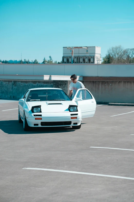 a man standing next to a white car in a parking lot, inspired by Zhu Da, unsplash, 1985 vector w8 twin turbo, seattle, 2 4 0 p footage, pantera ((countach))