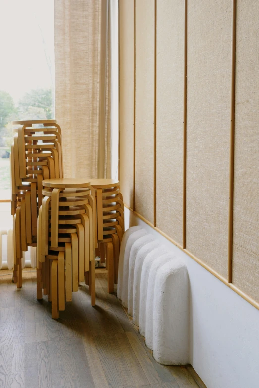 a room filled with wooden chairs and a radiator, inspired by Constantin Hansen, diffuse natural sun lights, straw, indoor soft lighting, stools