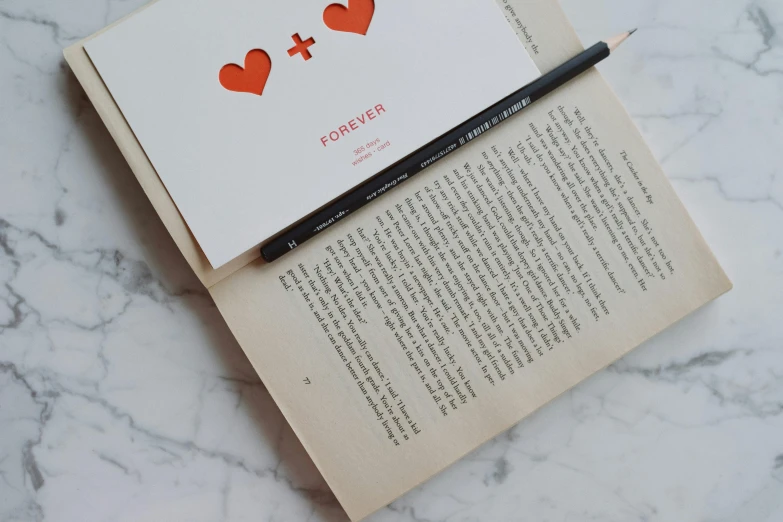 a pen sitting on top of an open book, an album cover, by Emma Andijewska, pexels contest winner, reading the book about love, pair of keycards on table, ffffound, holding pencil