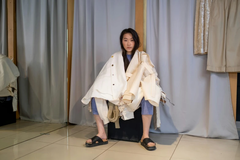 a woman sitting on top of a piece of luggage, inspired by Kim Tschang Yeul, unsplash, gutai group, dressed in an old white coat, wearing torn clothes, photo for a store, wearing a haori