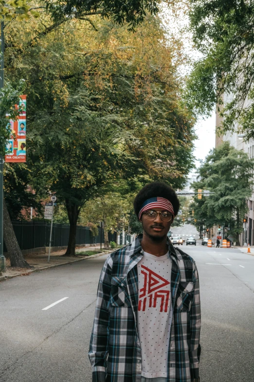 a man standing in the middle of a street, black arts movement, profile pic, trees around, downtown, high-res