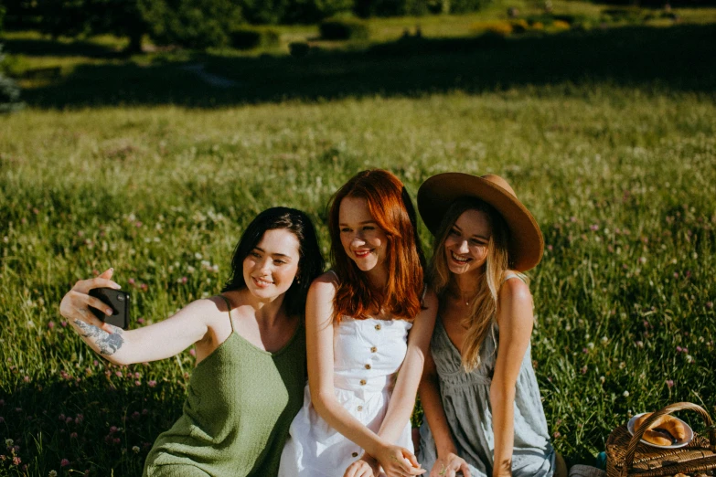 a group of women sitting on top of a grass covered field, pexels contest winner, ginger hair with freckles, avatar image, three women, selfie photo