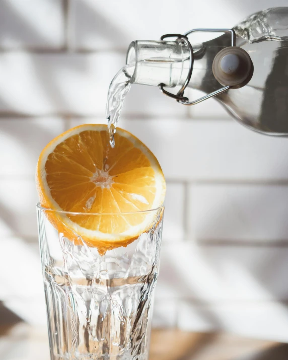 an orange being poured into a glass of water, pexels contest winner, lemon, afternoon hangout, bottle of vodka, looking off to the side