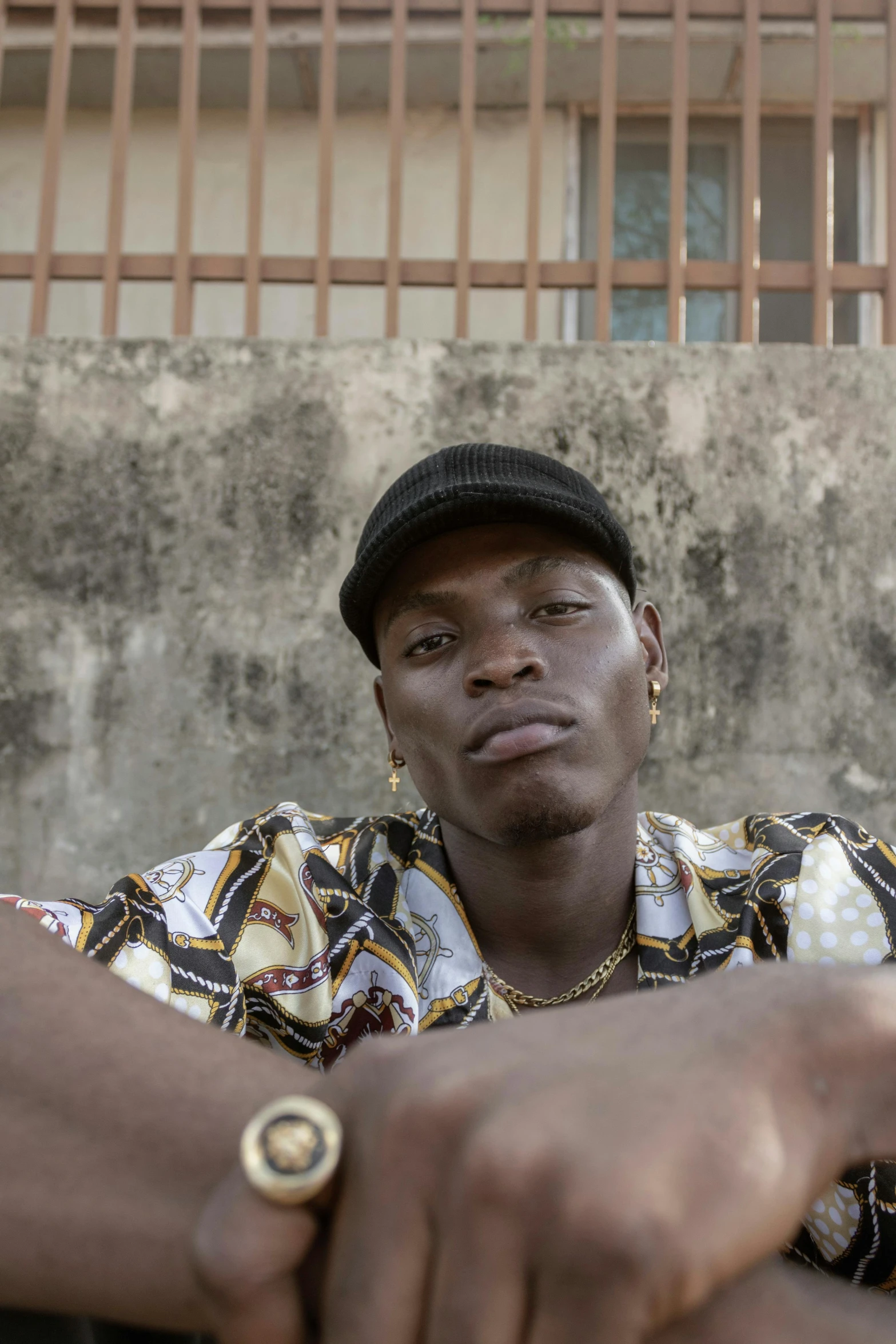 a man sitting on the ground in front of a building, adut akech, with rap cap on head, lgbtq, portait image