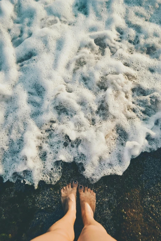 a person standing on top of a beach next to the ocean, trending on unsplash, renaissance, wet feet in water, foamy bubbles, laying on the ground, high angle shot