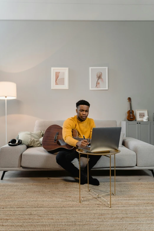 a man sitting on a couch using a laptop, an album cover, by Daniel Seghers, pexels contest winner, david uzochukwu, playing a guitar, product introduction photo, casually dressed