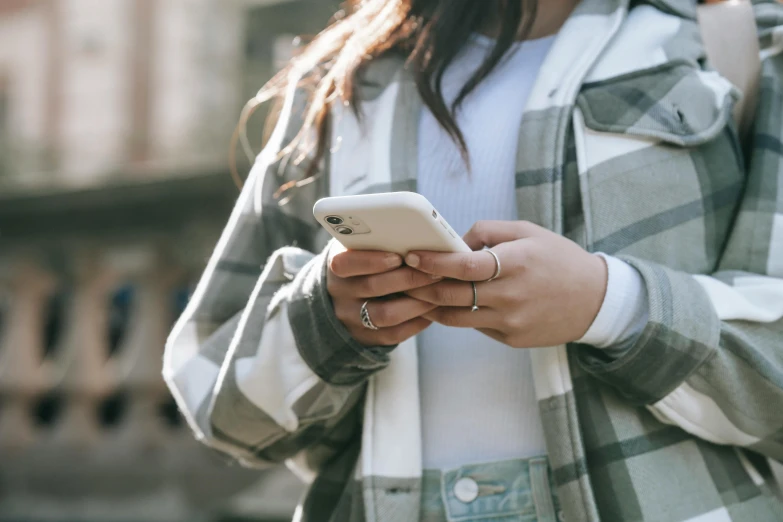 a close up of a person holding a cell phone, trending on pexels, white shirt and grey skirt, wearing a jeans jackets, wearing two metallic rings, mobile app