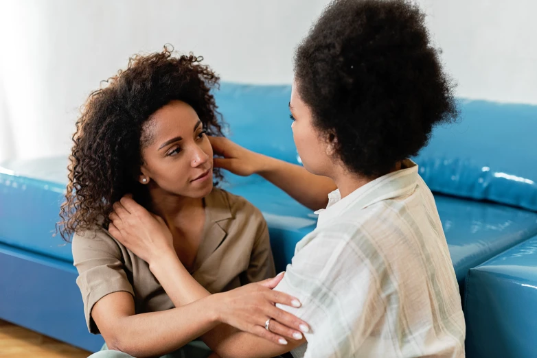 a woman sitting on top of a blue couch next to a man, by Everett Warner, trending on pexels, hurufiyya, comforting, woman holding another woman, with brown skin, tinnitus