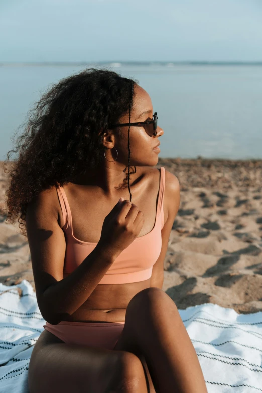 a woman sitting on a towel on the beach, trending on pexels, renaissance, light-brown skin, in shades of peach, curls, ( ( dark skin ) )
