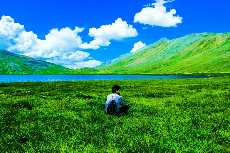 a man sitting on top of a lush green field, an album cover, pexels contest winner, mountain lake, blue and green colours, lonely scenery yet peaceful!!, khyzyl saleem