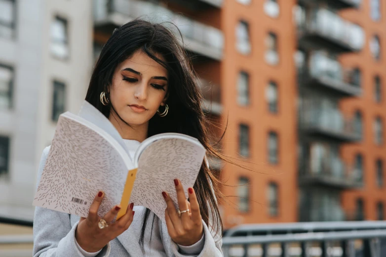 a woman sitting on a bench reading a book, trending on pexels, realism, indian girl with brown skin, on a rooftop, black haired girl wearing hoodie, vanessa morgan