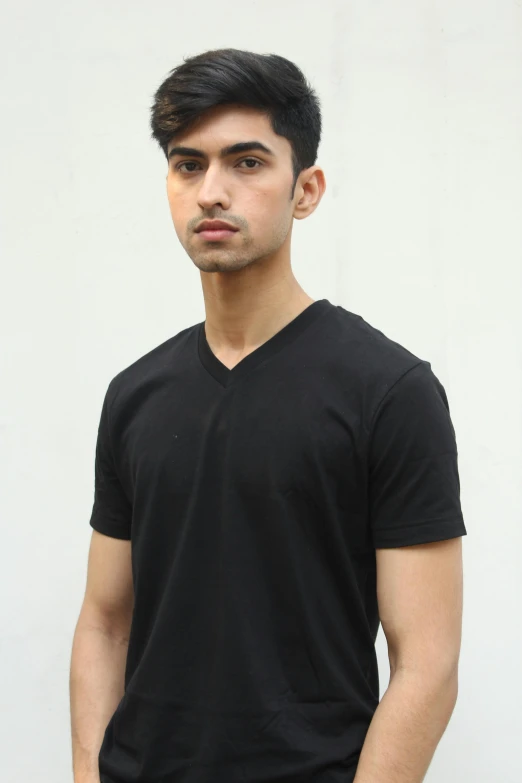 a young man standing in front of a white wall, by Robbie Trevino, pexels contest winner, wearing v - neck top, indian super model, wearing black tshirt, male teenager