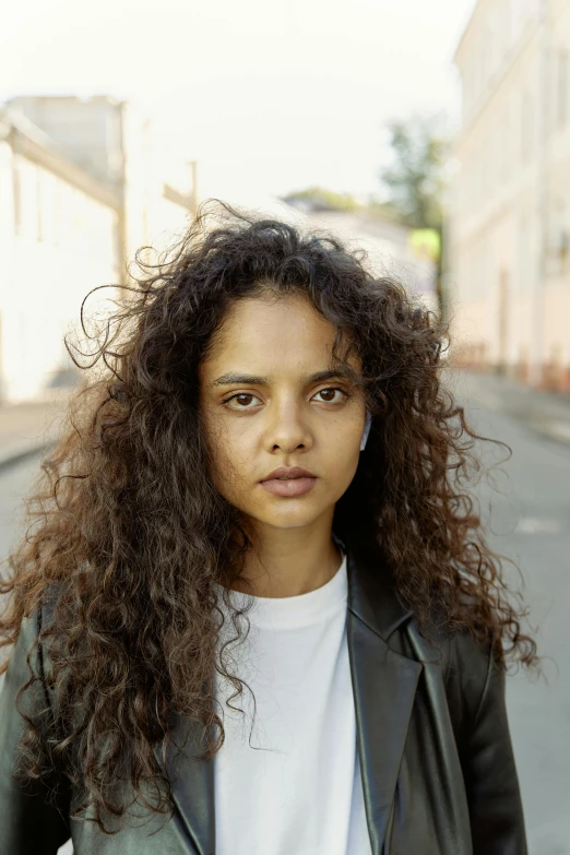 a woman standing in the middle of a street, by Sara Saftleven, pexels contest winner, photorealism, no makeup wavy hair, tessa thompson, young middle eastern woman, headshot