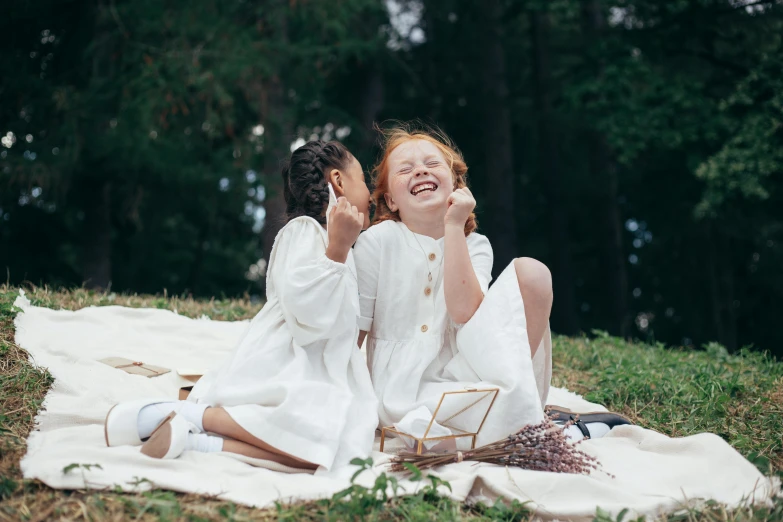 a couple of girls sitting on top of a blanket, by Emma Andijewska, pexels contest winner, girl in white dress dancing, laughing and joking, sadie sink, forest picnic