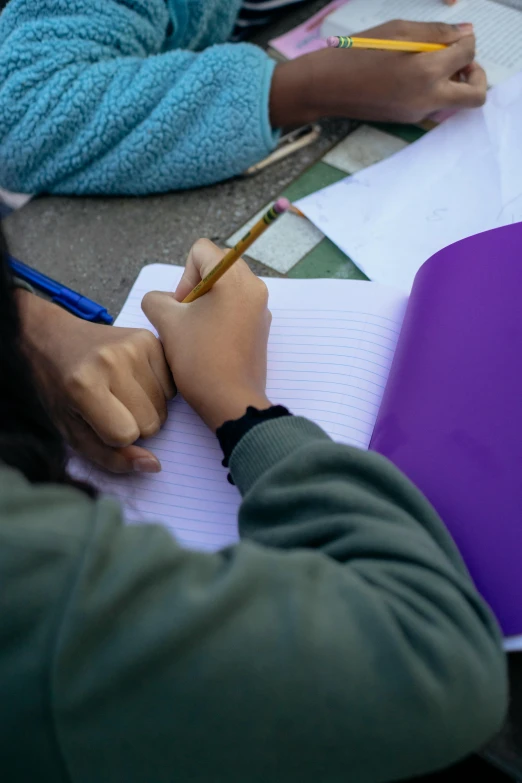 a group of people sitting at a table with notebooks and pencils, a child's drawing, by Carey Morris, trending on unsplash, young man in a purple hoodie, outside on the ground, high angle close up shot, high quality photo