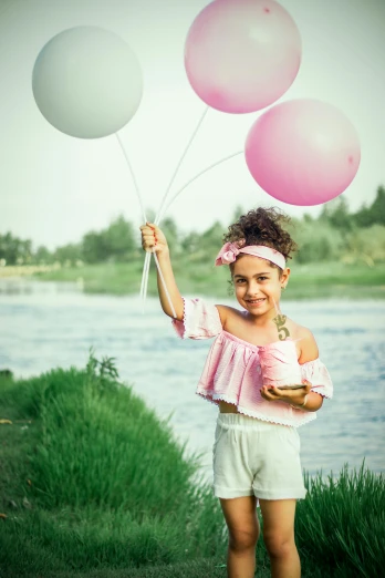 a little girl holding a bunch of pink and white balloons, a colorized photo, pexels contest winner, lake view, modeling shoot, ameera al-taweel, pastel clothing