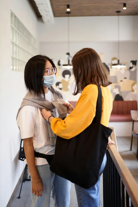 a couple of women standing next to each other, a picture, by Jang Seung-eop, trending on unsplash, happening, wearing facemask, holding a gold bag, in a coffee shop, facing each other