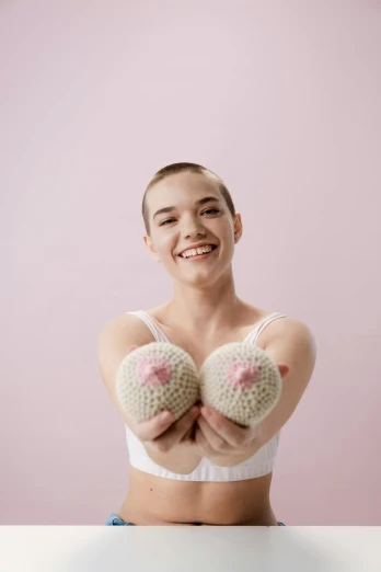 a woman sitting at a table with two crocheted hearts in her hands, an album cover, by Annabel Eyres, featured on reddit, happening, posing together in bra, partially bald, puffballs, pose(arms up + happy)