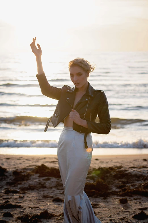 a woman standing on top of a sandy beach, an album cover, inspired by Winona Nelson, leather jacket, pale skin!, summer sunlight, emilia clarke