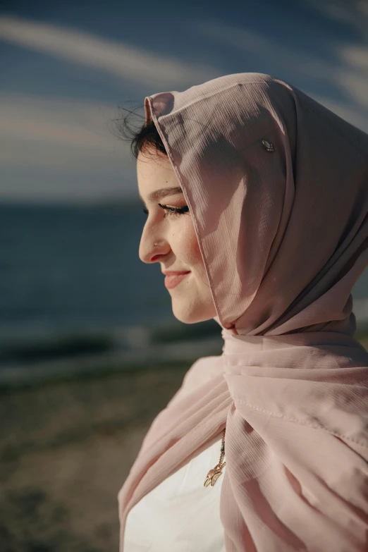 a woman standing on top of a beach next to the ocean, inspired by Nazmi Ziya Güran, hurufiyya, close - up on face, **cinematic, shawl, pink