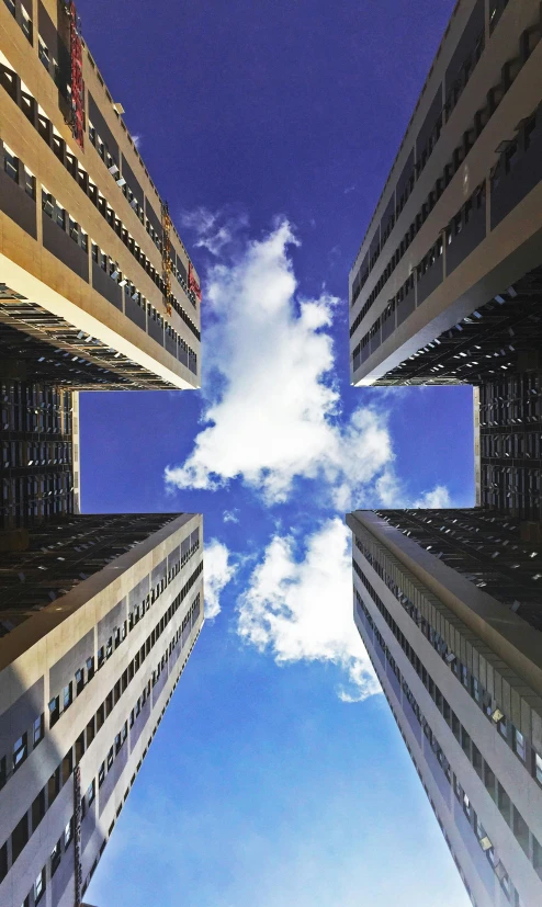 a group of tall buildings with a blue sky in the background, an album cover, inspired by Leandro Erlich, unsplash, in sao paulo, coherent symmetrical artwork, volumetric clouds, four stories high
