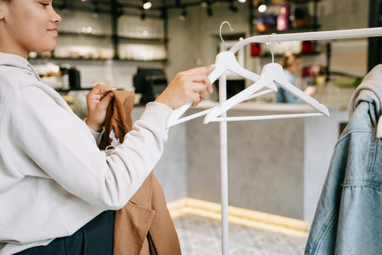 a woman looking at clothes on hangers in a clothing store, by Nicolette Macnamara, trending on pexels, wearing a white winter coat, standing in a restaurant, holding a staff, slightly minimal