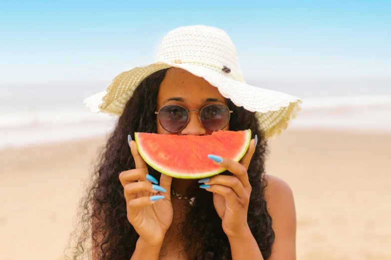 a woman eating a slice of watermelon on the beach, pexels contest winner, brown skinned, black sun hat, woman with rose tinted glasses, 1 2 9 7