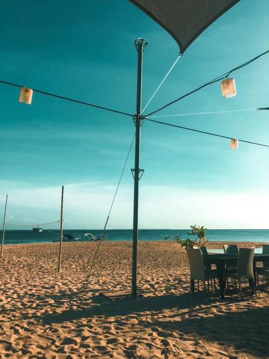 a table and chairs sitting on top of a sandy beach, skies, hanging lanterns, trending on vsco, thumbnail