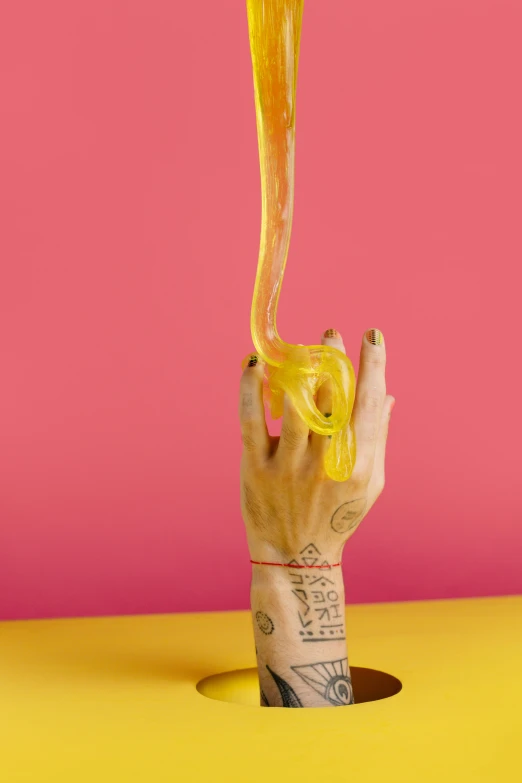 a hand holding a cup with liquid pouring out of it, by Nathalie Rattner, conceptual art, noodles, pink and yellow, super long shot, bong