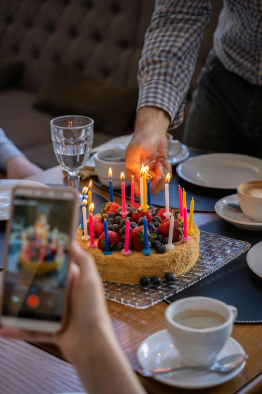 a person taking a picture of a birthday cake, a colorized photo, by Dan Content, pexels, vegetables on table and candle, on, where a large, celebrating