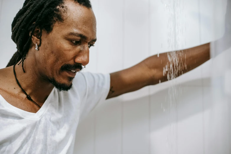 a man with dreadlocks standing in front of a wall, trending on pexels, process art, under a shower, hydration, man in white t - shirt, recovering from pain