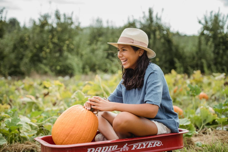 a woman sitting in a wagon holding a pumpkin, pexels contest winner, white straw flat brimmed hat, avatar image, isabela moner, gardening