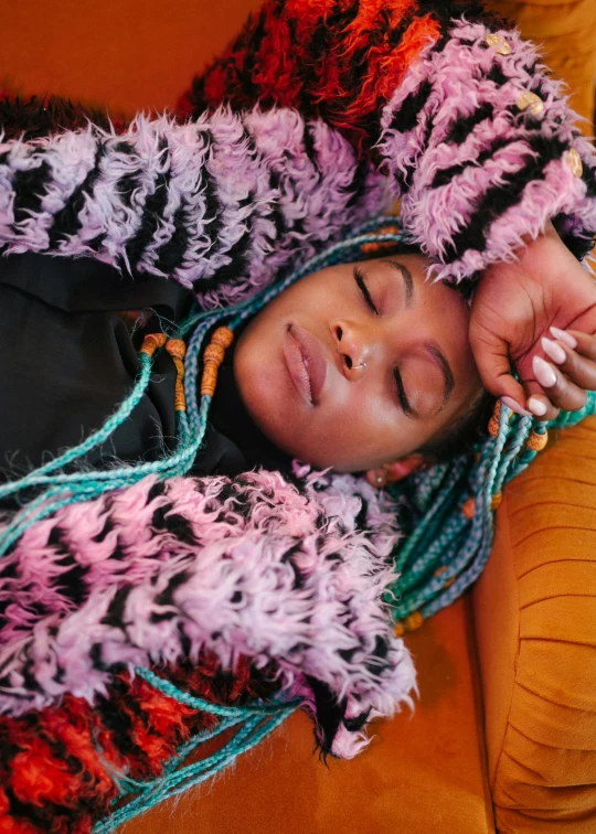 a close up of a person laying on a couch, afrofuturism, colorful clothes, sleepy feeling, long black braids, model wears a puffer jacket