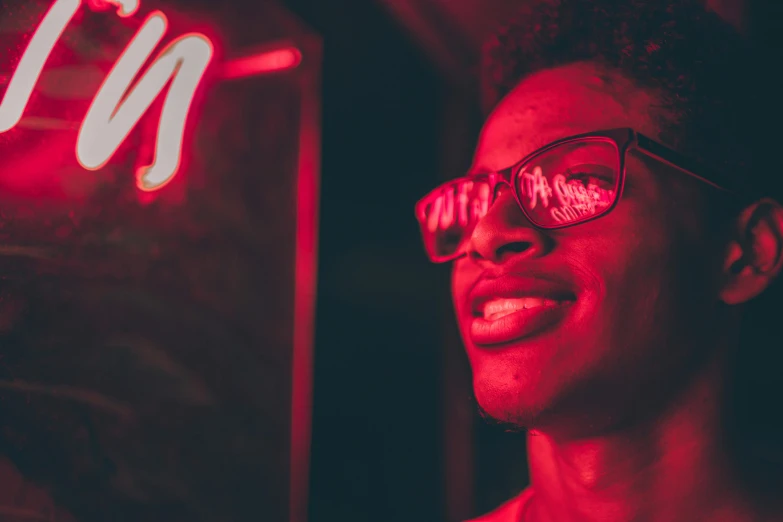 a man wearing glasses standing in front of a neon sign, pexels contest winner, funk art, red glowing skin, smiling seductively, black teenage boy, in a strip club