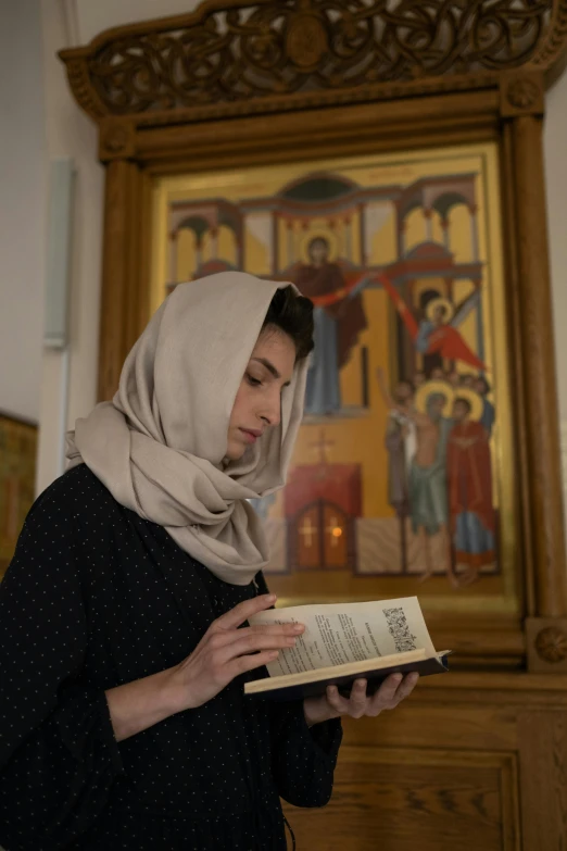 a woman reading a book in front of a painting, a picture, shutterstock, qajar art, in a church. medium shot, hijab, orthodox icons, high quality screenshot