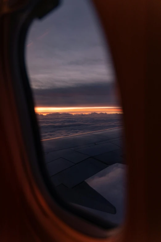 a view out of an airplane window at sunset, happening, looking partly to the left, overcast dusk, the window is open, orange glow