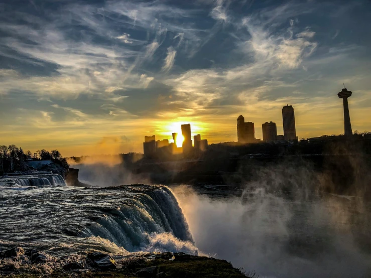 a sunset over a waterfall with a city in the background, by Greg Rutkowski, pexels contest winner, niagara falls, slide show, islamic, conde nast traveler photo