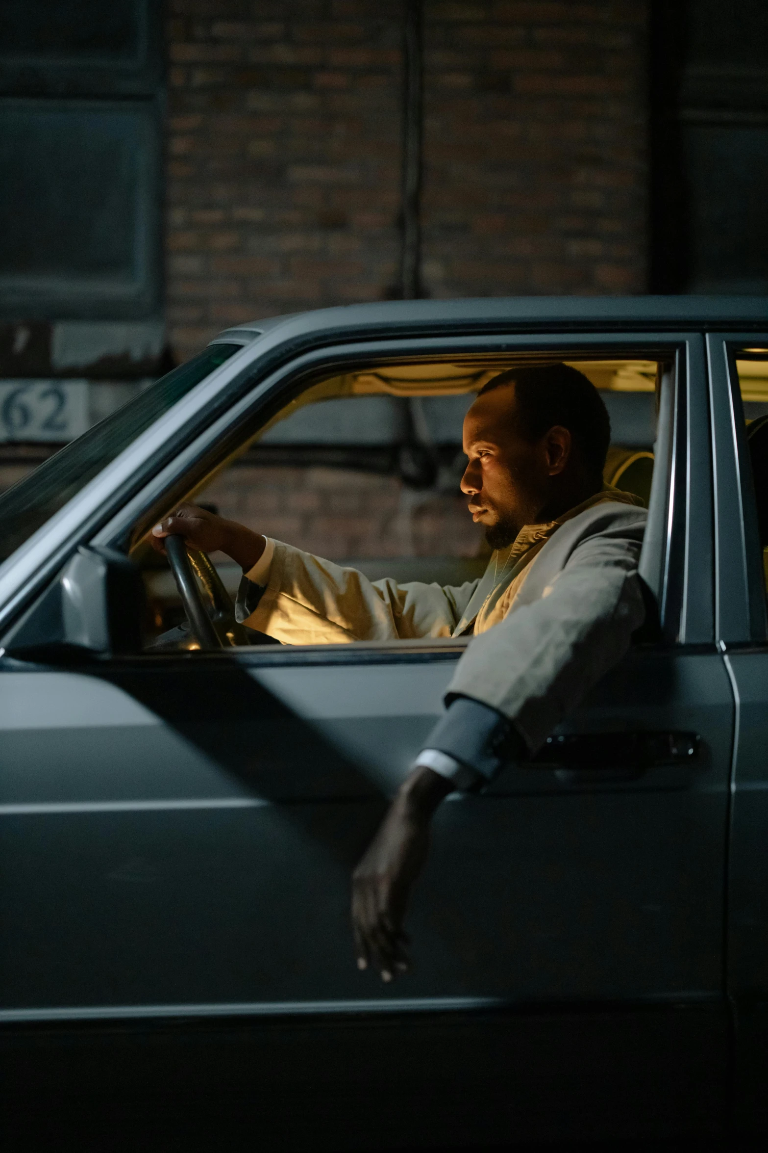 a man sitting in the driver's seat of a car, inspired by Gordon Parks, realism, dark-skinned, 8 k movie still, square, [ theatrical ]