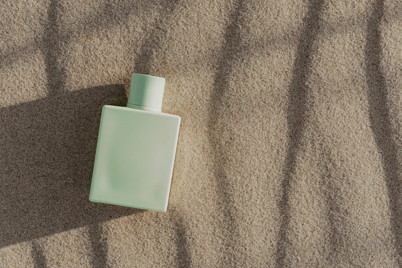 a bottle of perfume sitting in the sand, inspired by Raoul De Keyser, unsplash, conceptual art, pastel green, rectangle, ignant, sunbathed skin