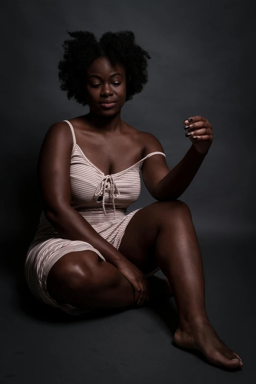 a woman sitting on the ground holding a cigarette, by Lily Delissa Joseph, dark skin tone, muted colored bodysuit, studio medium format photograph, fit curvy physique