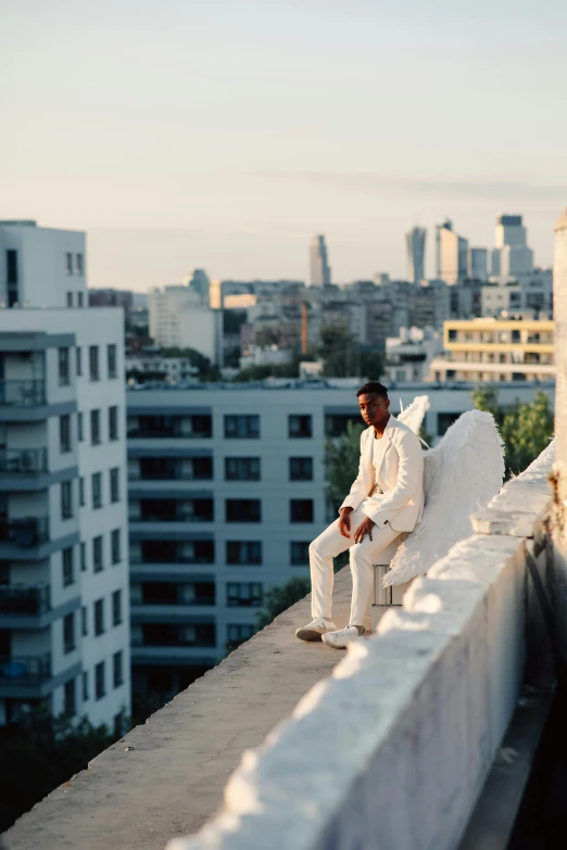 a man in a white suit sitting on a ledge, by Barthélemy Menn, unsplash, happening, roof garden, slide show, high angel distant shot, late afternoon