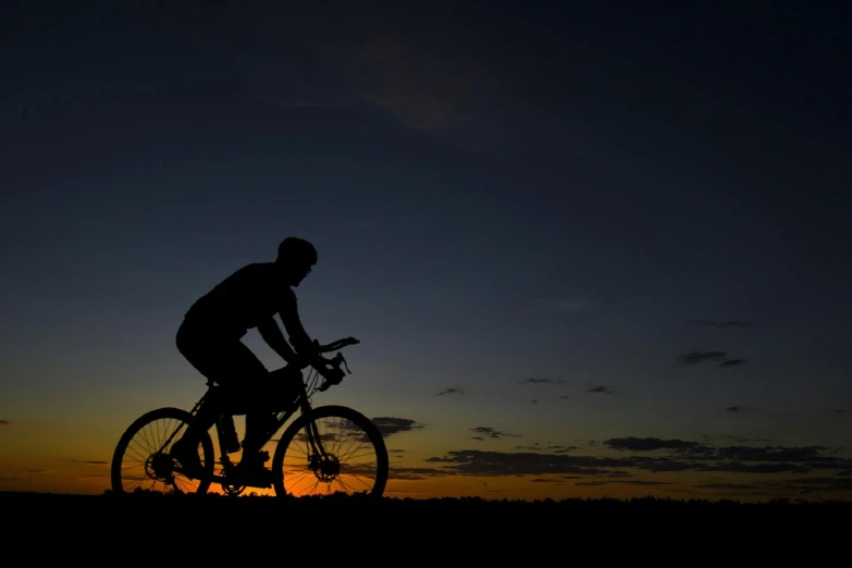 a silhouette of a person riding a bike at sunset, in the dark, avatar image