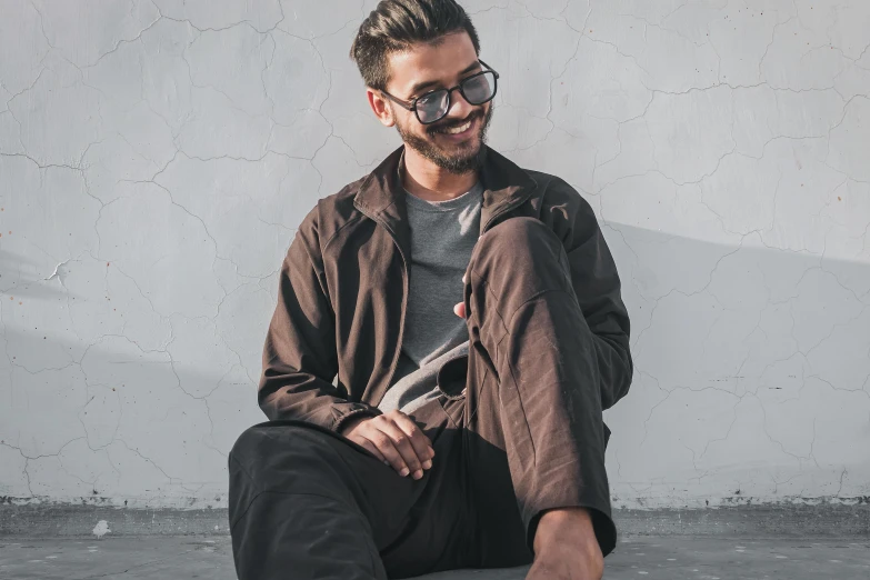 a man with glasses sitting on a skateboard, inspired by Ismail Acar, pexels contest winner, hurufiyya, wearing cargo pants, brown jacket, relaxing and smiling at camera, avatar image