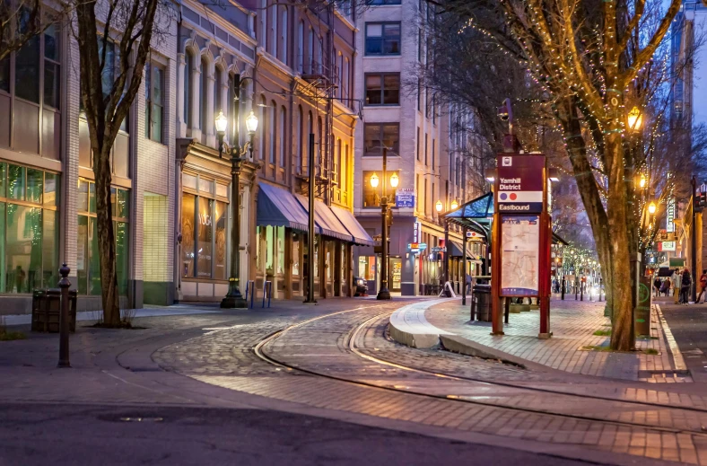 a train traveling down a city street next to tall buildings, by Meredith Dillman, pexels contest winner, art nouveau, warm street lights store front, cascadia, square, panoramic shot