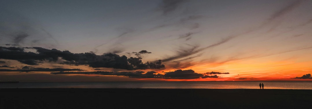 a person standing on a beach at sunset, unsplash contest winner, minimalism, panorama view of the sky, dark grey and orange colours, red clouds, heath clifford