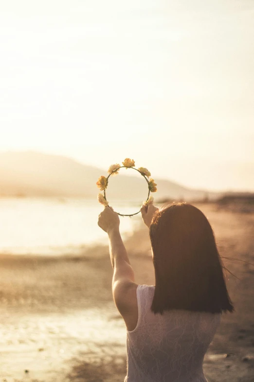 a woman standing on top of a beach holding a frisbee, inspired by Oleg Oprisco, pexels contest winner, romanticism, looking into a mirror, holding flowers, clear and sunny, (golden hour)